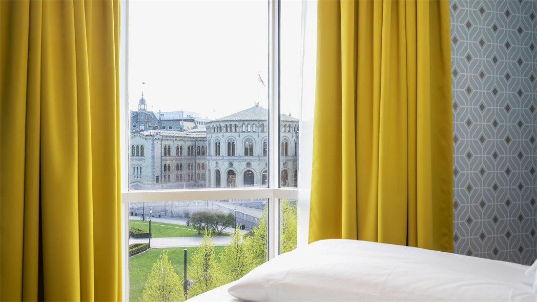 Gule gardiner og store vinduer med utsikt over Stortinget i junior suite på Thon Hotel Cecil