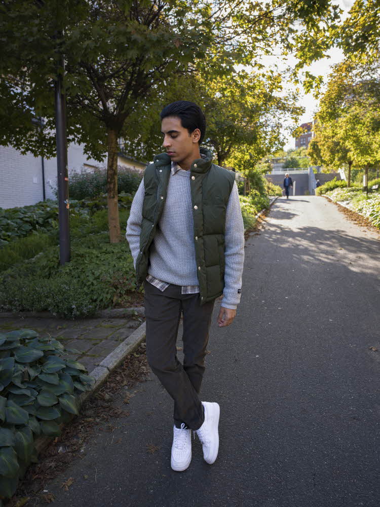 Gutt i grønn boblevest, blå genser, rutete skjorte, blå bukser og hvite sneakers.