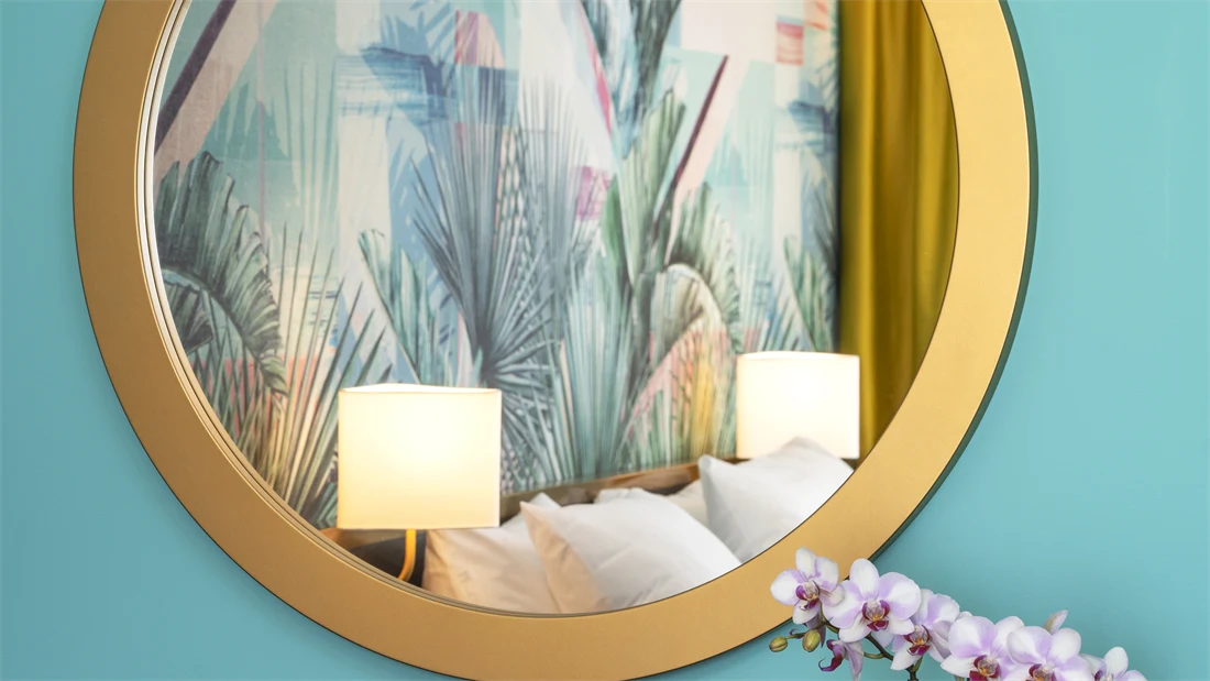 Rundt speil som reflekterer seng og tapet på rom på Thon Hotel Storo