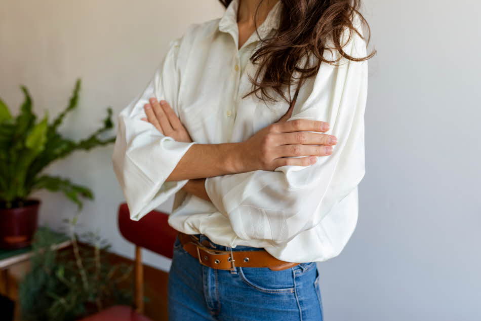 Nærbilde av dame med hvit skjorte og jeans stående med hendene i kors