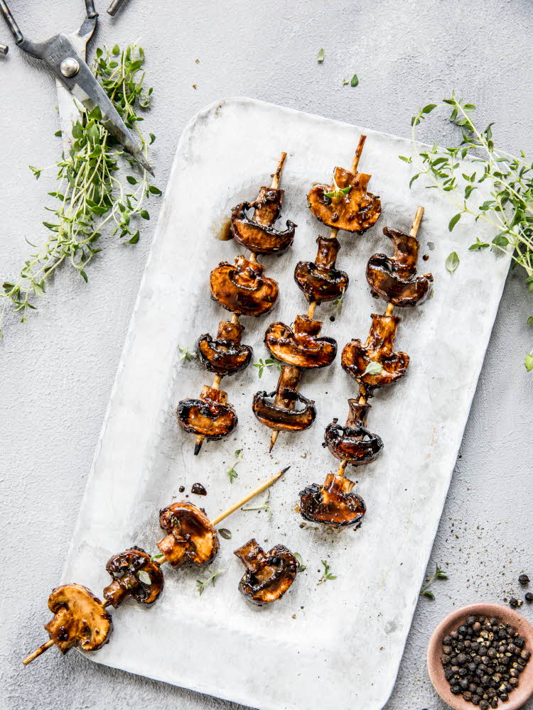 Grillspyd med grillet sopp på hvitt fat med urter rundt