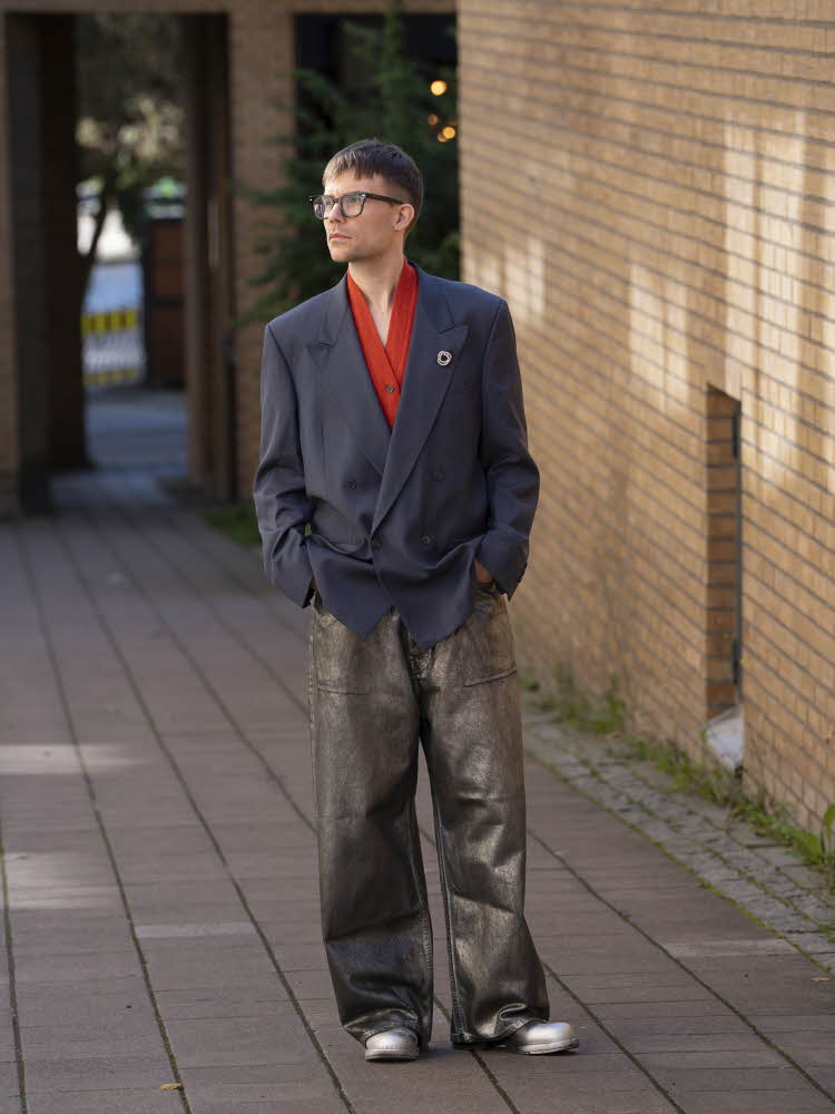 Mann i rød topp, blå blazer, sølvfarget jeans og sølvfargede sko.