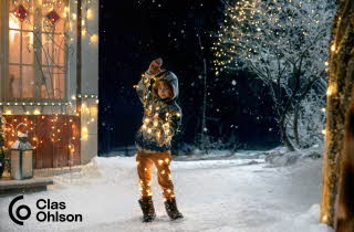 En gutt som står surret i en lyslenke ute i snøen.