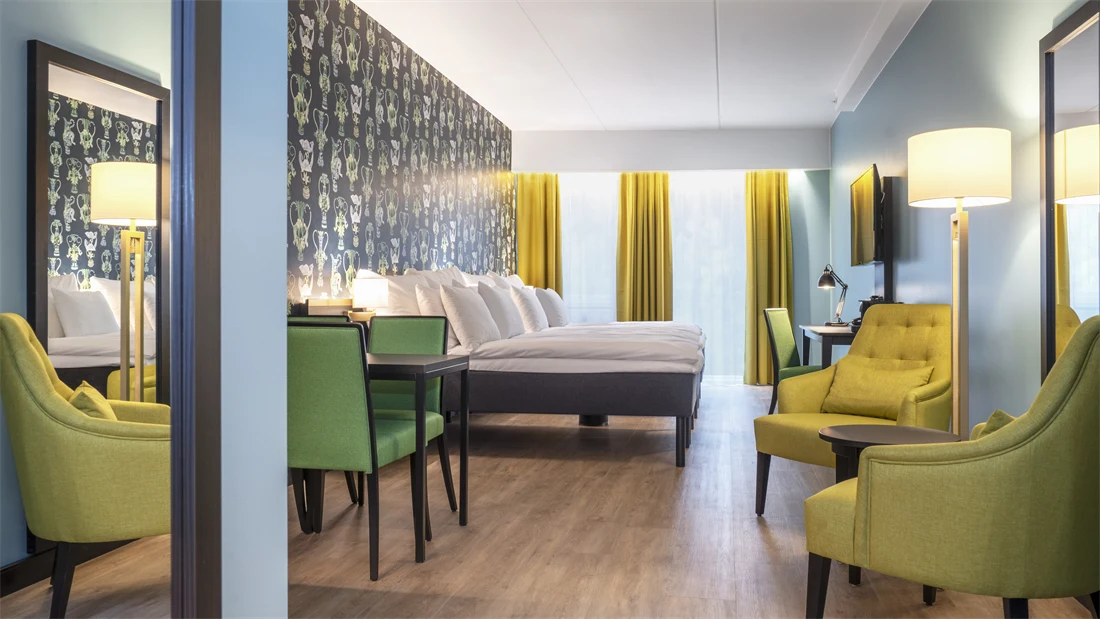 Sittegruppe med gule stoler, to dobbeltsenger og spisebord med grønne stoler i junior suite på Thon Hotel Linne