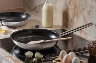 Kjøkken med to stekepanner, egg og melk på benken.