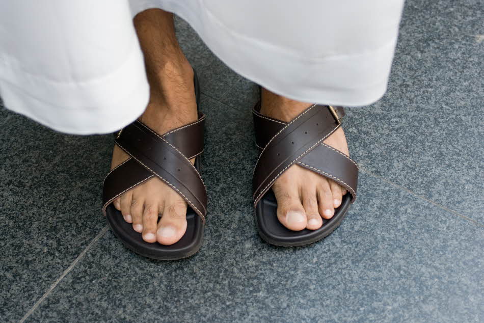 Nærbilde av manneføtter med brune skinnsandaler og hvit bukse