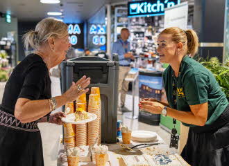 Senterleder Christina på AMFI Vågsbygd står bak en bod og deler ut kaffe og kake til senterkunder