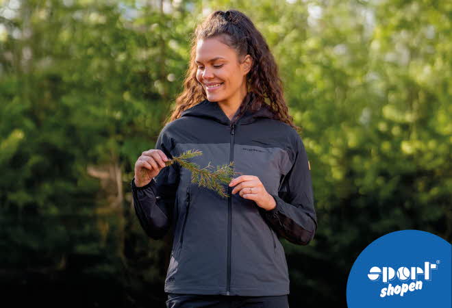 Dame med langt krøllete hår holder en gren i grønn natur.