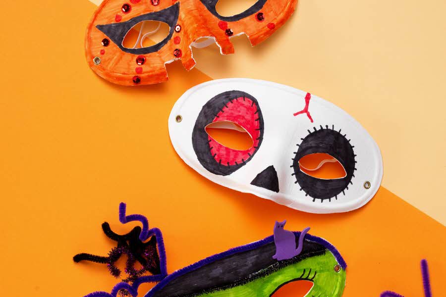 Tre Halloweenmasker ligger på en oransje bakgrunn