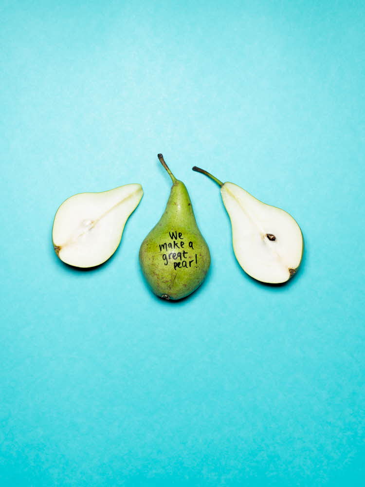 En hel og en halv pære som ligger på turkis bakgrunn. På den ene pæren er det skrevet med sort tusj "We make a great pear" 