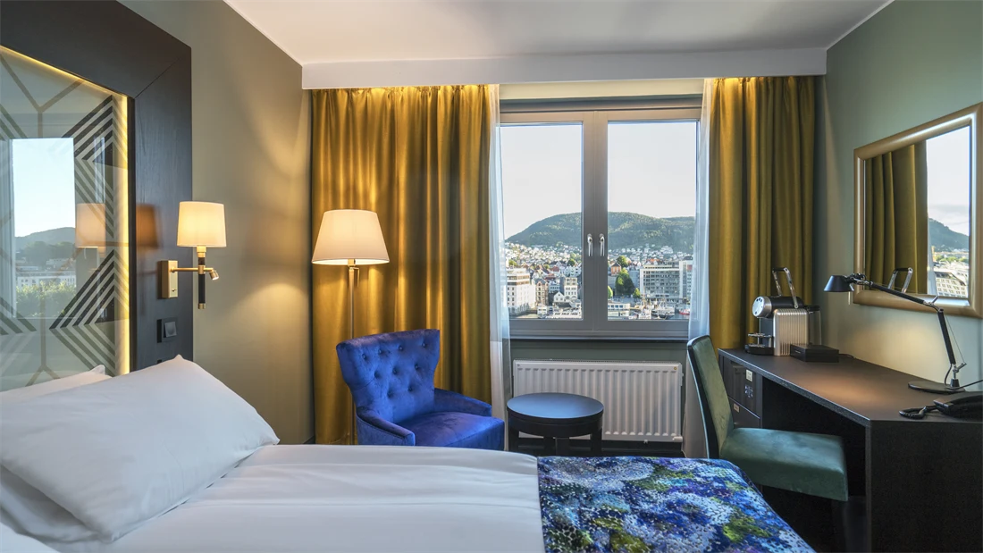 Dobbeltseng med stol, skrivebord og smart-TV i superiorrom på Thon Hotel Orion i Bergen sentrum med utsikt over Bergen Brygge.