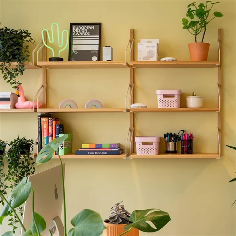 Detaljer fra vegg på kontor med gule vegger, grønne planter og vegghengt hylle med hjemmekoselige ting.