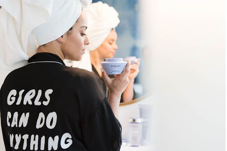 Dame i morgenkåpe og håndkle på hodet og som holder et Kerastase hårprodukt i hånden