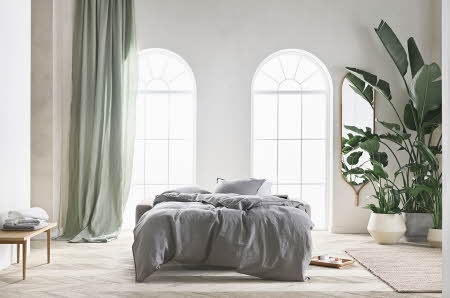 stort og lys stue med grå sovesofa, grønn plante og gardiner