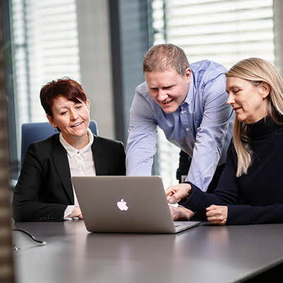 tre kollegaer som ser sammen på en pc skjerm på et møterom