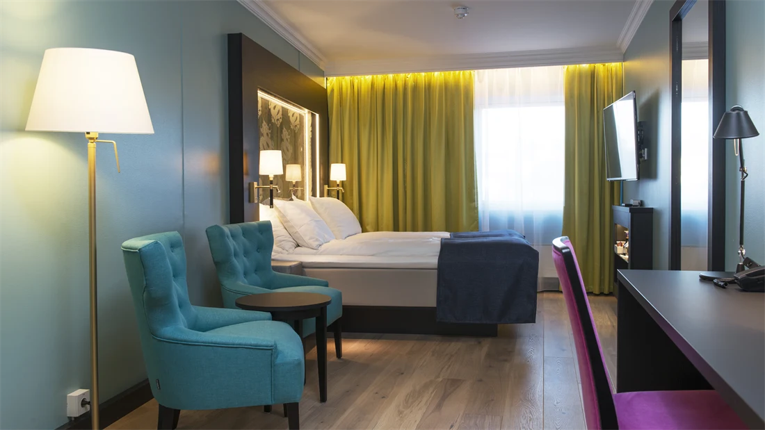Dobbeltseng blå lenestol, gule gardiner, skrivepult med lilla stol og dragemlnster på seng på Thon hotel Terminus i Oslo sentrum nær Jernbanetorget