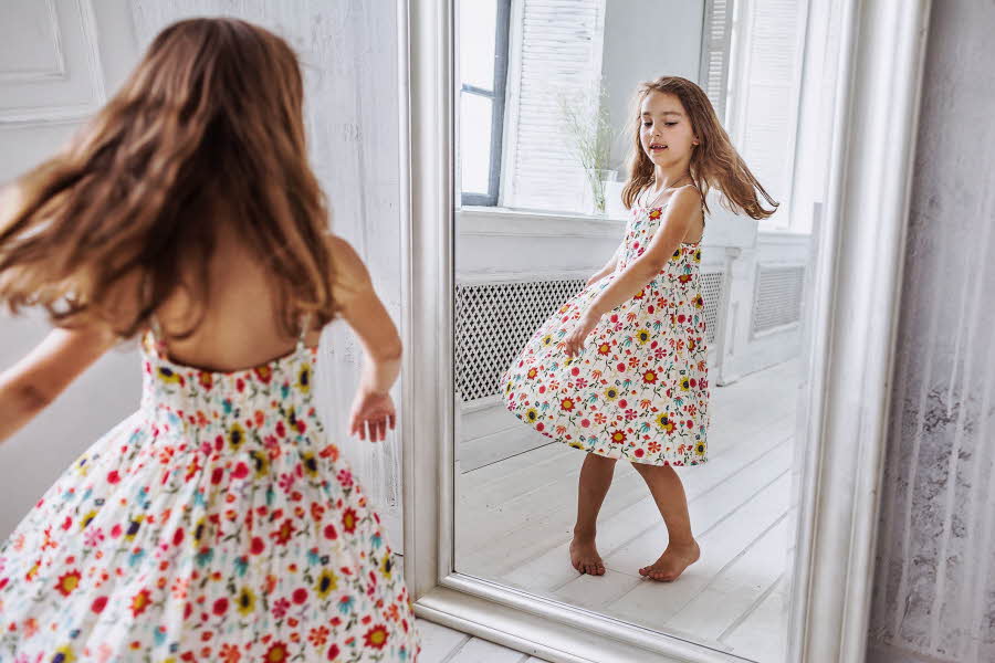 Jente danser i blomstrete kjole foran speilet