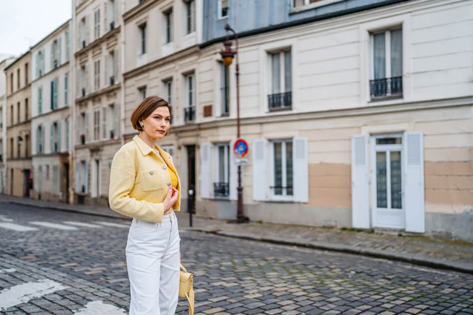 Dame med gul tweedjakke, hvit jeans og gul beske poserer på gate i Paris