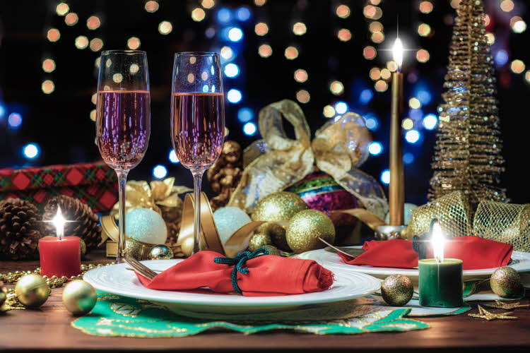 Bord som er pyntet til nyttårsfest, med røde servietter, julekuler, lys og to champagneglass. Foto til artikkel om hvordan du fikser nyttårsfest uten å slite deg helt ut.