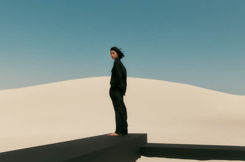 En kvinne som står på en sanddyne ikledd sorte klær