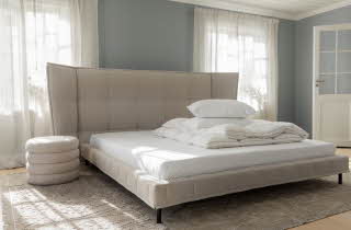 En stor seng med sengegavel, med en dyne og pute brettet oppe på