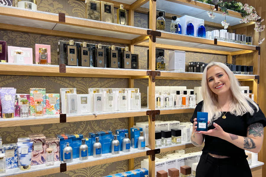 Kvinnelig butikkansatt på Fredrik & Louisa holder en parfyme foran en hylle med produkter