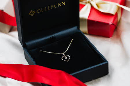 Et gullsmykke med hjerte anheng som ligger i en Gullfunn boks