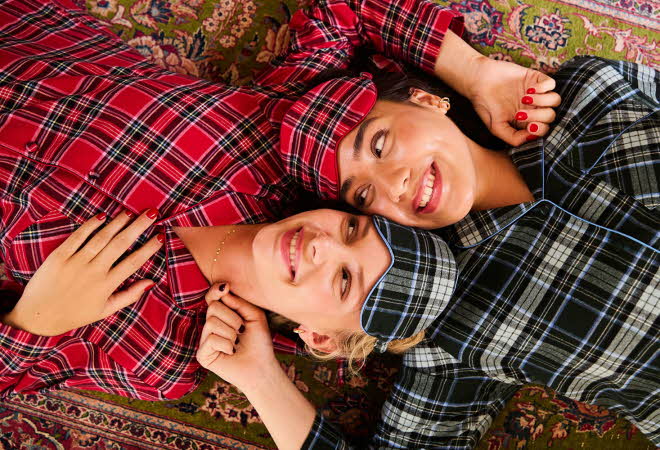 To damer ligger på et teppe iført rutete pysjamas i rødt og blått mønster.