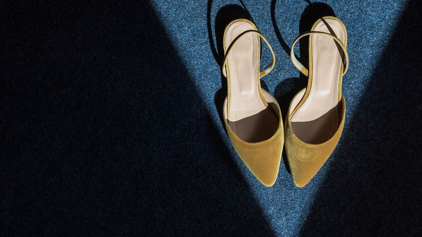 Spisse slingback-sandaler i okerfarget fløyel. Står i en trekant av lys. Illustrasjonsbilde til artikkel om vårmote for sko.
