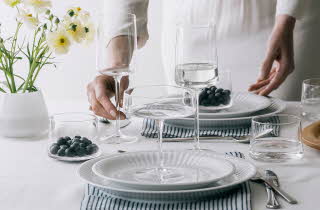 Dekket bord med glass, tallerkener, servietter og blomsterdekorasjon.