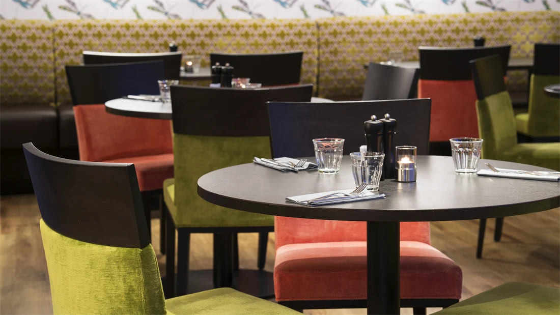 Runde bord omkranset av olivengrønne og lyserøde stoler i Thon Hotel Skis frokostsal