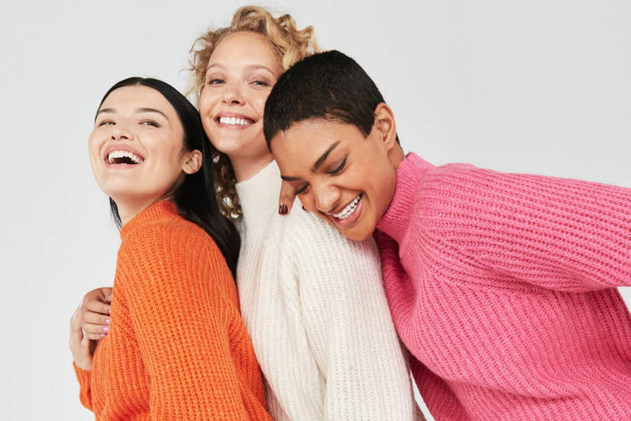 tre damer som poserer sammen i oransje, hvit og rosa genser