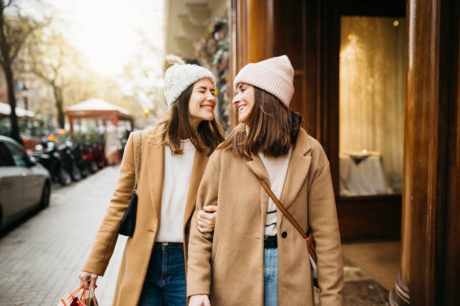 To jenter i beige kåpe smiler mot hverandre på gata