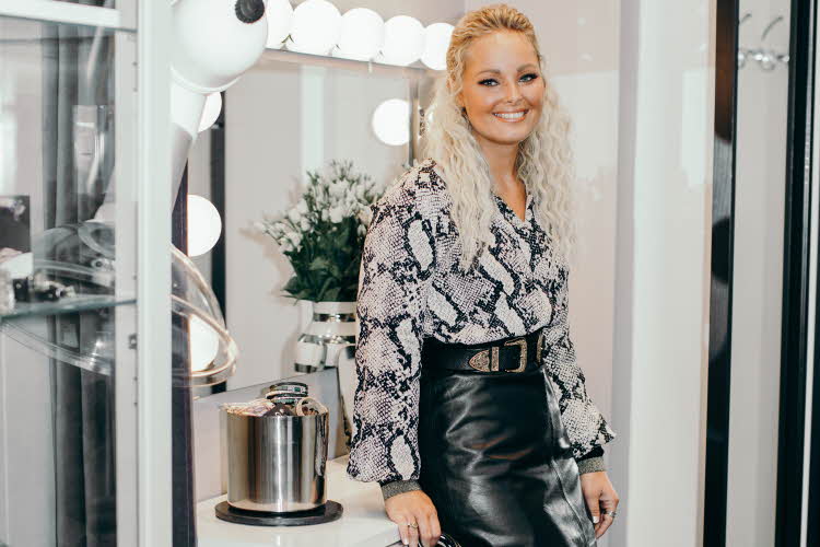 Janne Celin står iført bluse med slangeprint, et skinnskjørt og statement belte