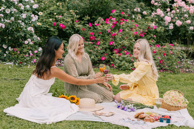 Tre damer som har piknik i en hage