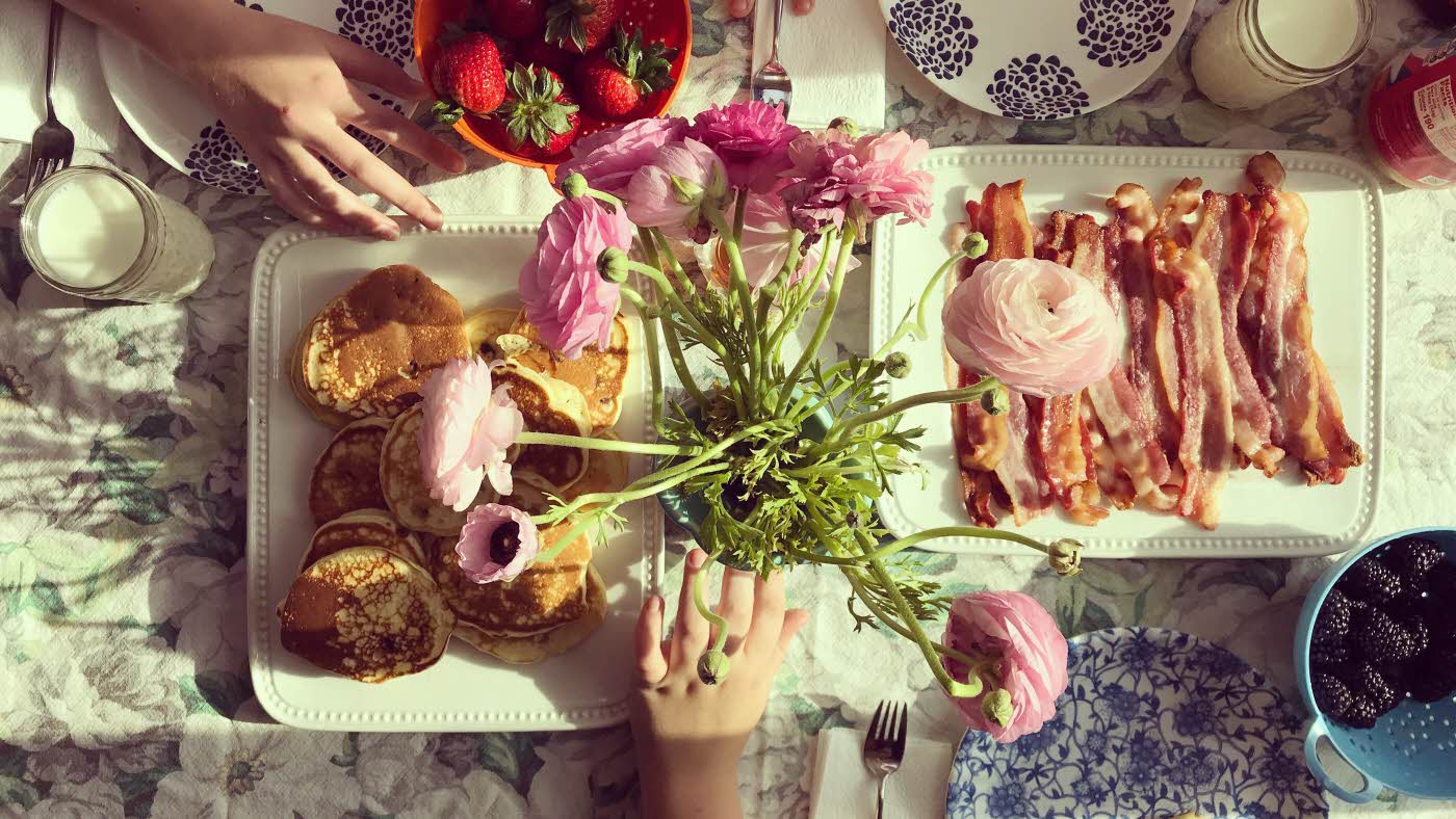 Frokostbord med rosa blomster, bacon og pannekaker