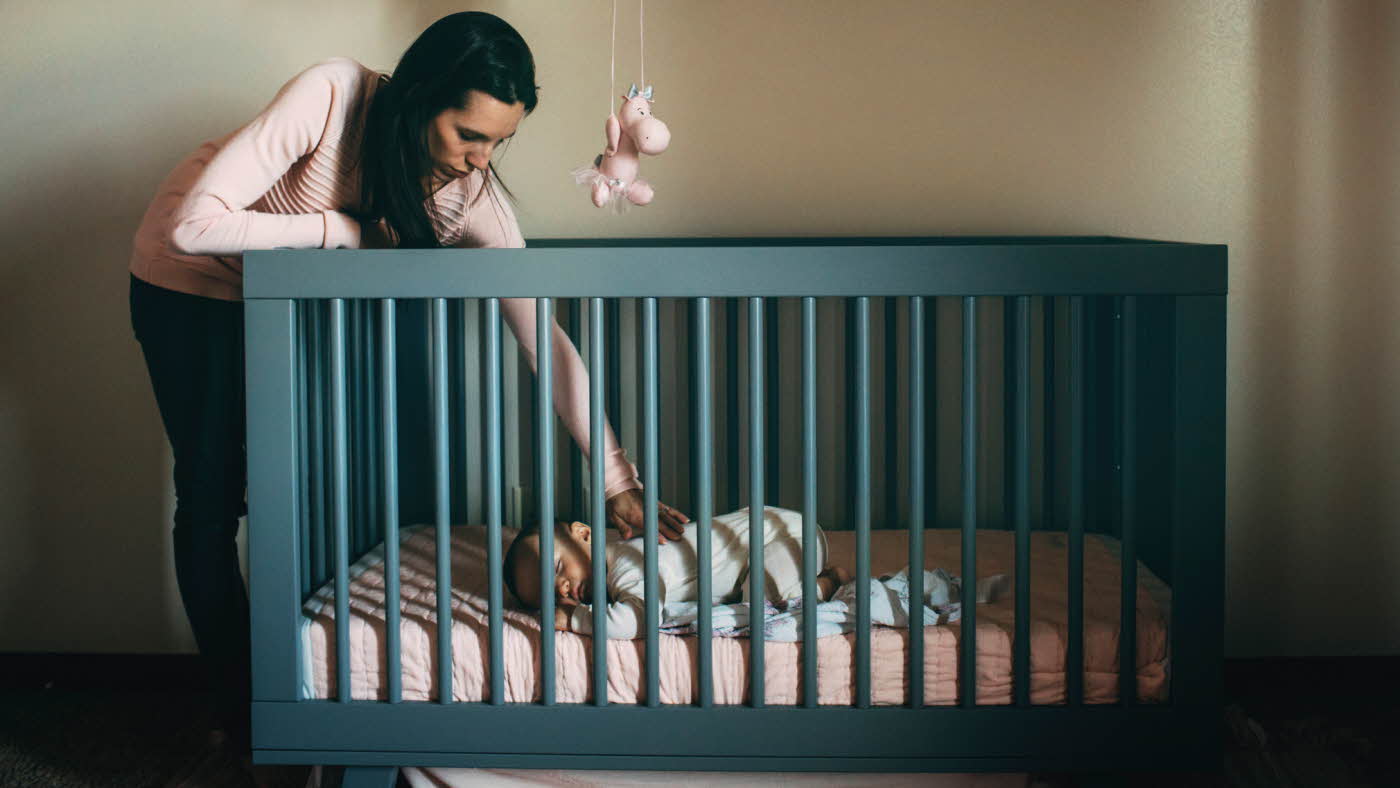 Liten baby ligger i seng med mor som lener seg over