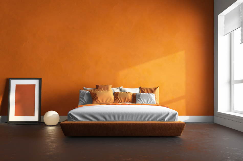 Soverom med oransje vegg, hvitt sengeteppe og oransje puter.