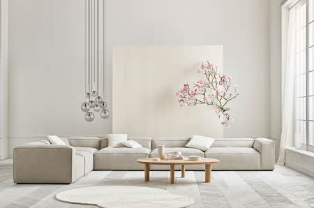 stue med stor lys sofa, hengende lys, stuebord, teppe og et tre med rosa blomster