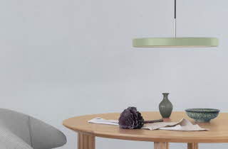 Et bord med en stol, som har en rund, flat lampe som henger fra taket over det