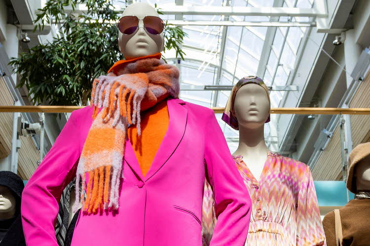 Utstillingsdukke med solbriller, stort fargerikt skjerf, oransje topp og rosa dressjakke