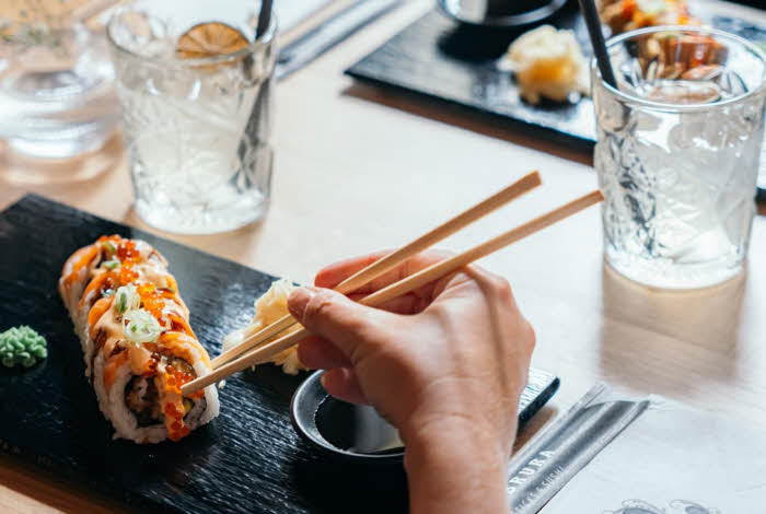 Bilde av en hånd som holder spisepinner og sushi