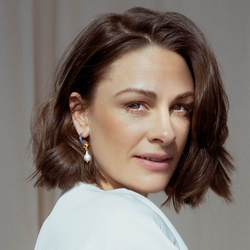 Jenny Skavlan med hvit skjorte og lilla øreringer