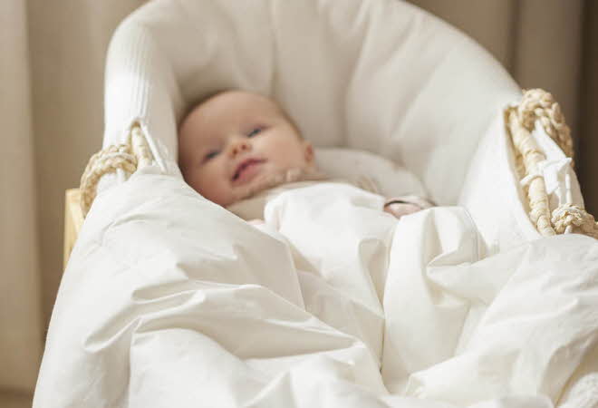 En smilende baby som ligger i en hvit babykurv.