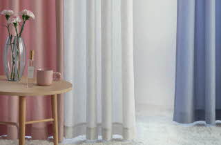 Tre Lena gardiner i forskjellige farger, med et lite bord med vase og blomster på