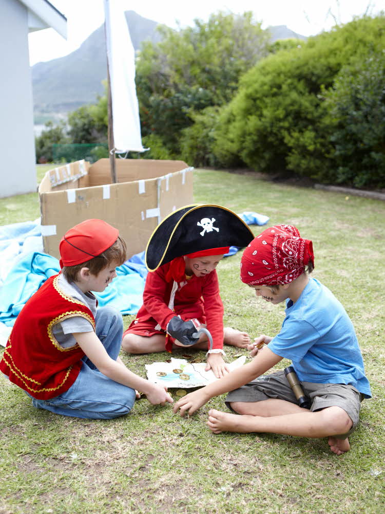 Tre barn utkledd som pirater, sitter på gresset rundt et skattekart