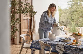 En kvinne står og fikser en plante i en vase på et bord ute