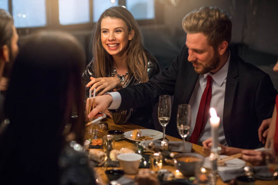 Mann med mørk dress, lys skjorte og rødt slips sitter i et middagsselskap