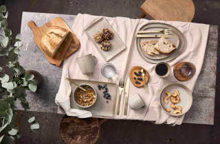 Et bord sett ovenfra dekket med Aida RAW servise, brød, bær og frokostblanding