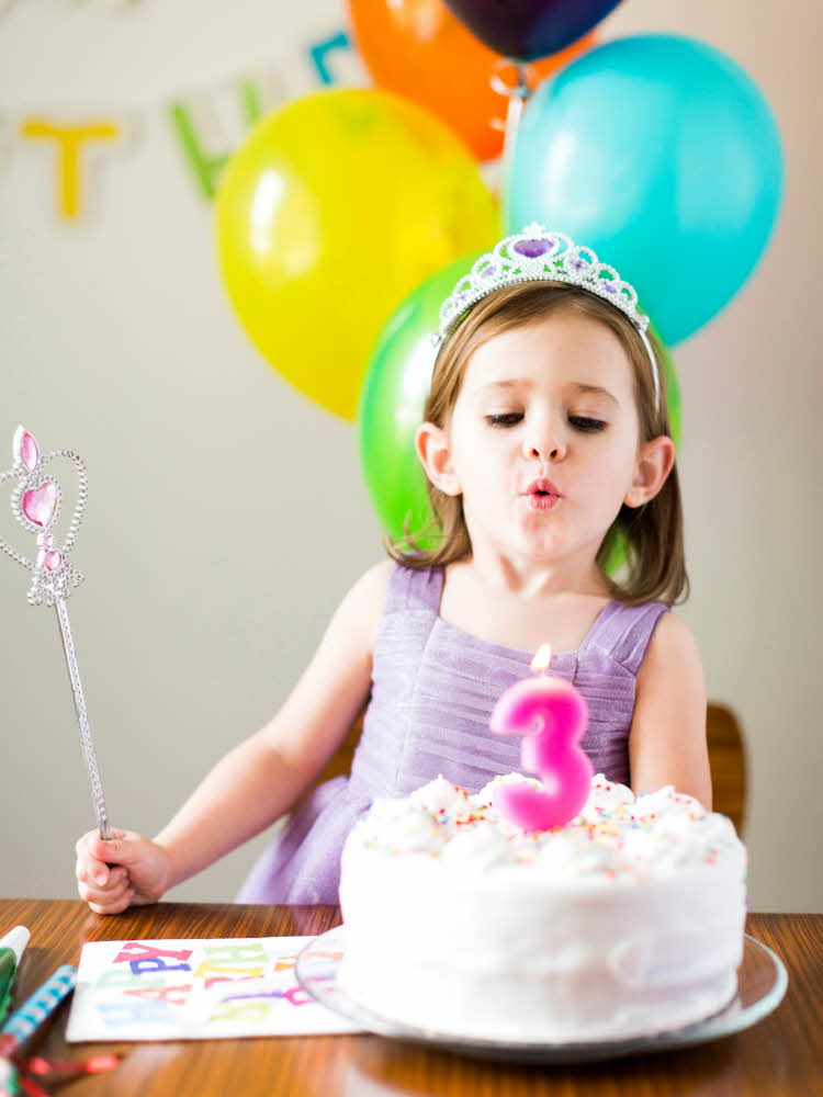 Jente med krone som blåser ut lys på kake Nærbilde av en rosa cupcake på en rosa tallerken